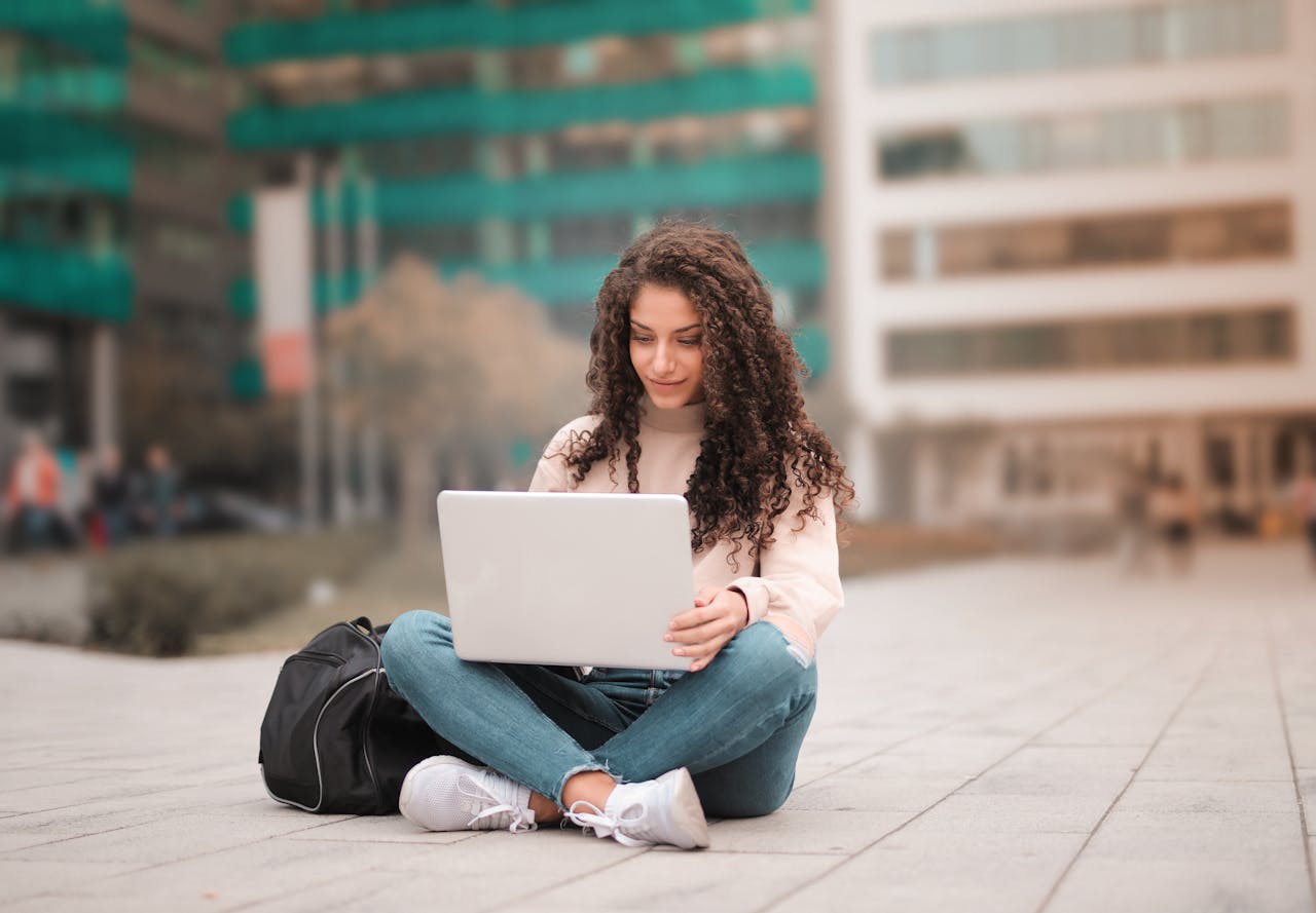 services-09 A woman with curly hair using a laptop while sitting outdoors, showcasing modern remote work lifestyle.