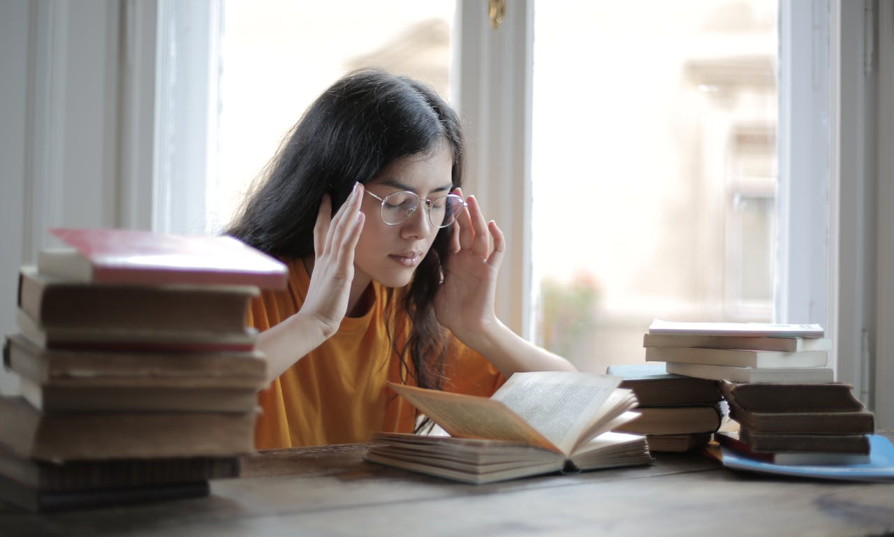 services-05 A young woman feeling fatigued while reading and studying surrounded by books.