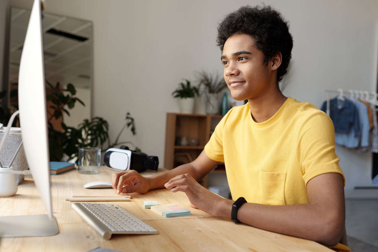 services-06 Teenager smiling while studying online at home. Modern education setup with computer and VR headset.